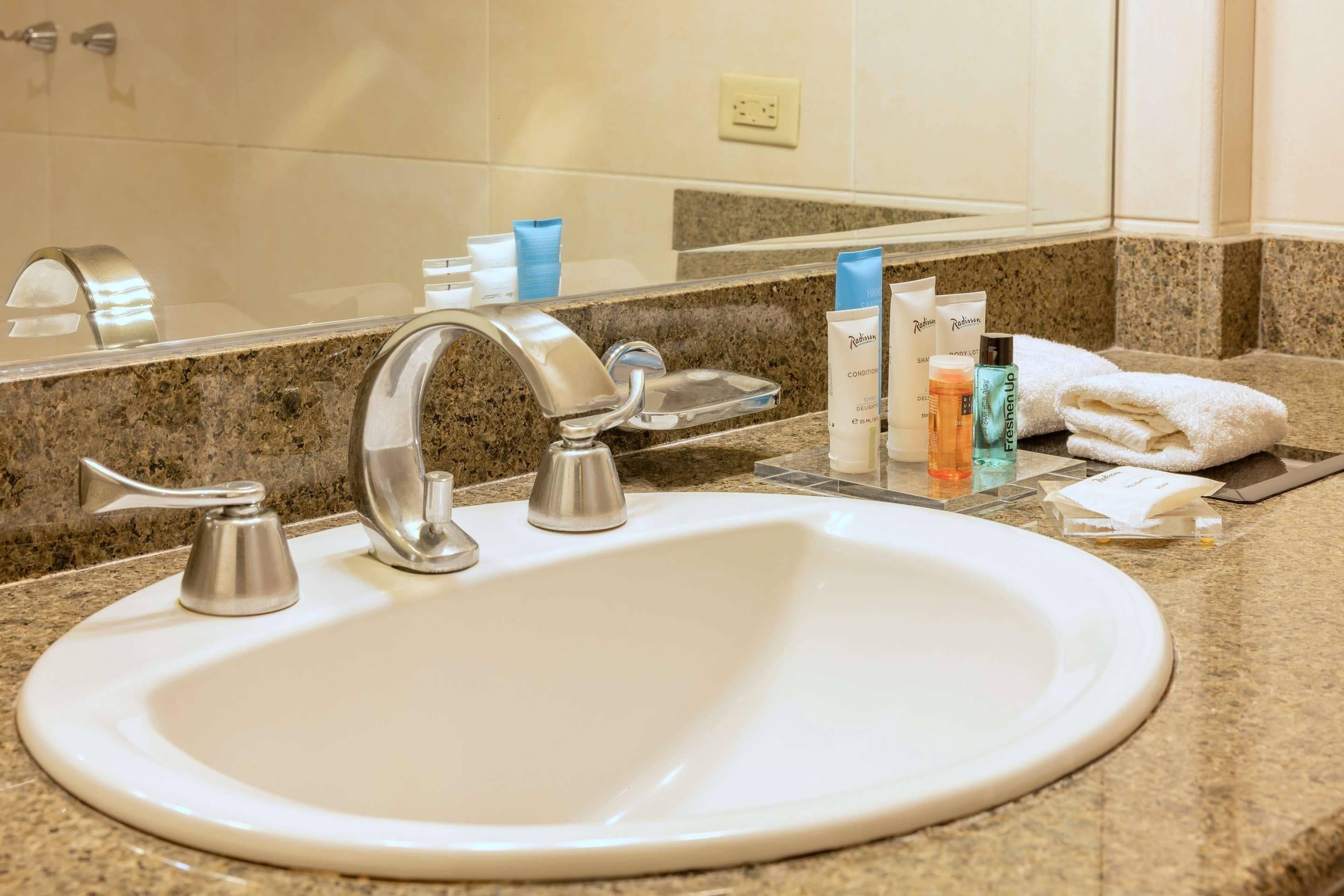 A bathroom with a white sink, a mirror, and toiletries on the counter.