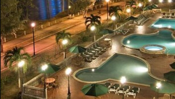 Un resort con piscina, sillones de descanso y vista a un puente por la noche.