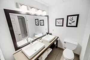 Um banheiro moderno com três pias, um espelho grande e um vaso sanitário.