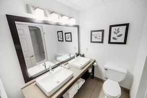 A modern bathroom with three sinks, a large mirror, and a toilet.