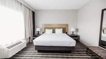 Habitación de hotel con una cama grande, dos mesitas de noche con lámparas, un banco, un radiador y un espejo grande en la pared.
