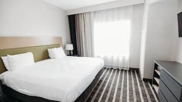 A hotel room with a large bed, a nightstand with a lamp, a dresser, and a window with curtains.