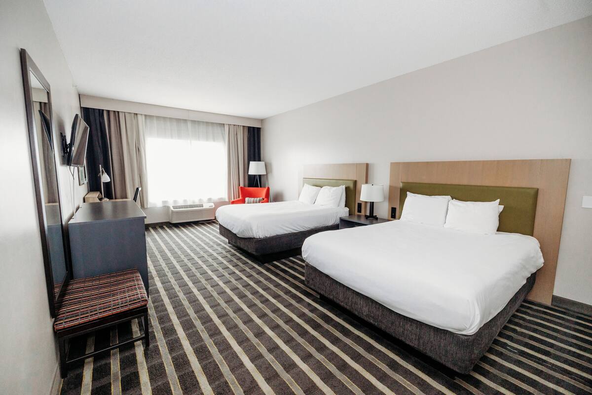 Ett hotellrum med två sängar, ett skrivbord, en stol, en TV och ett fönster med gardiner.