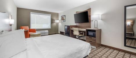 A hotel room with a large bed, a desk with a computer, a chair, a TV, and a window.