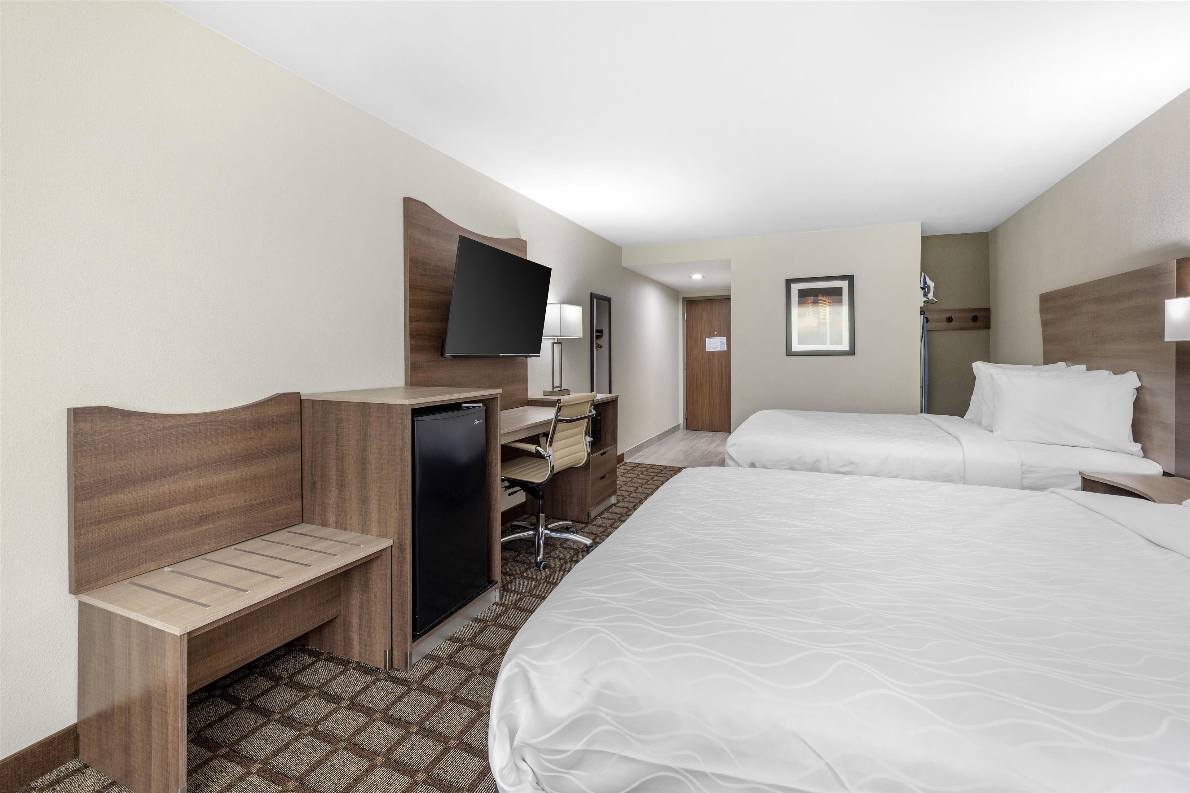 A hotel room with two beds, a desk, a television, and a small refrigerator.