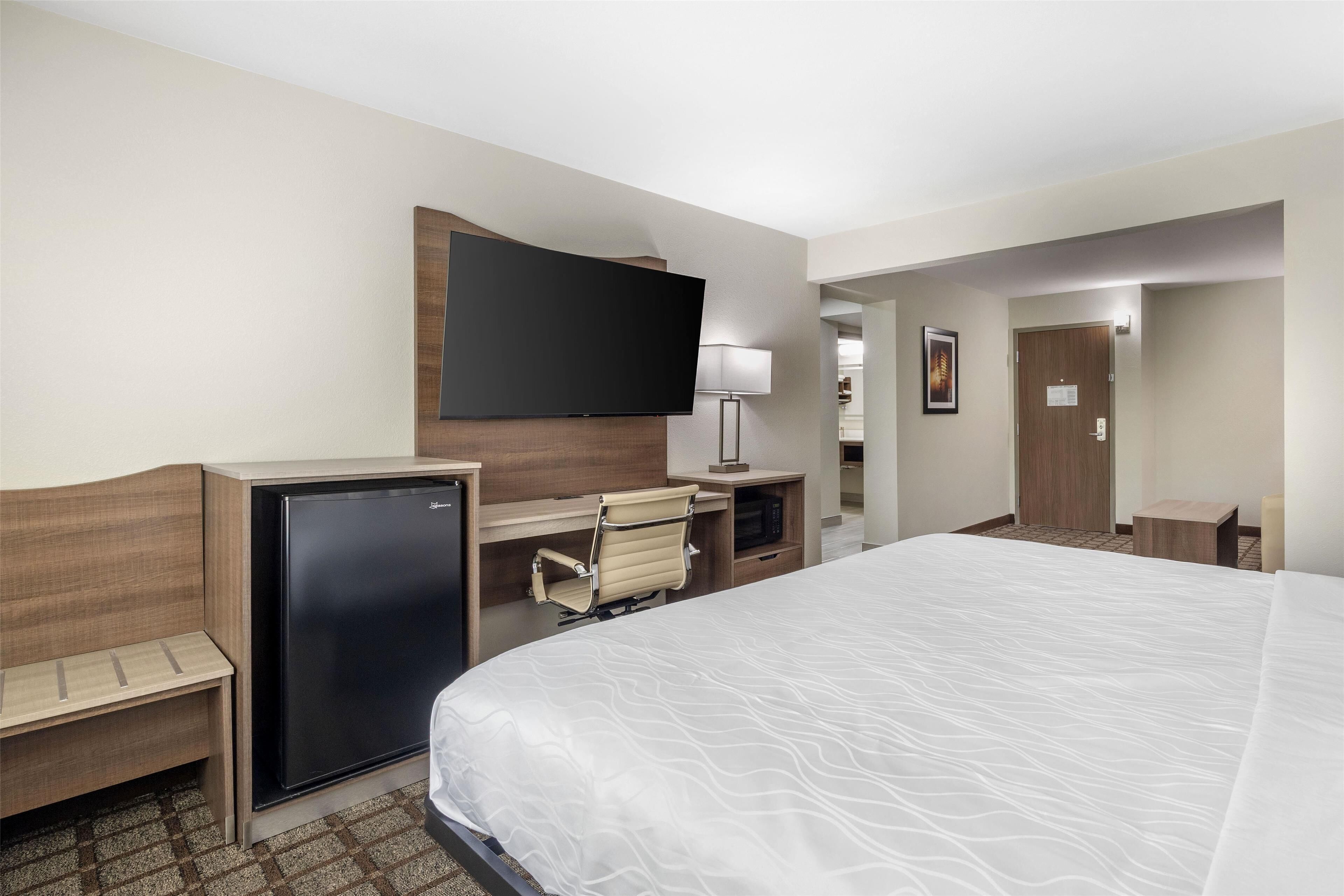 A hotel room with a bed, a desk with a computer, a television, and a refrigerator.