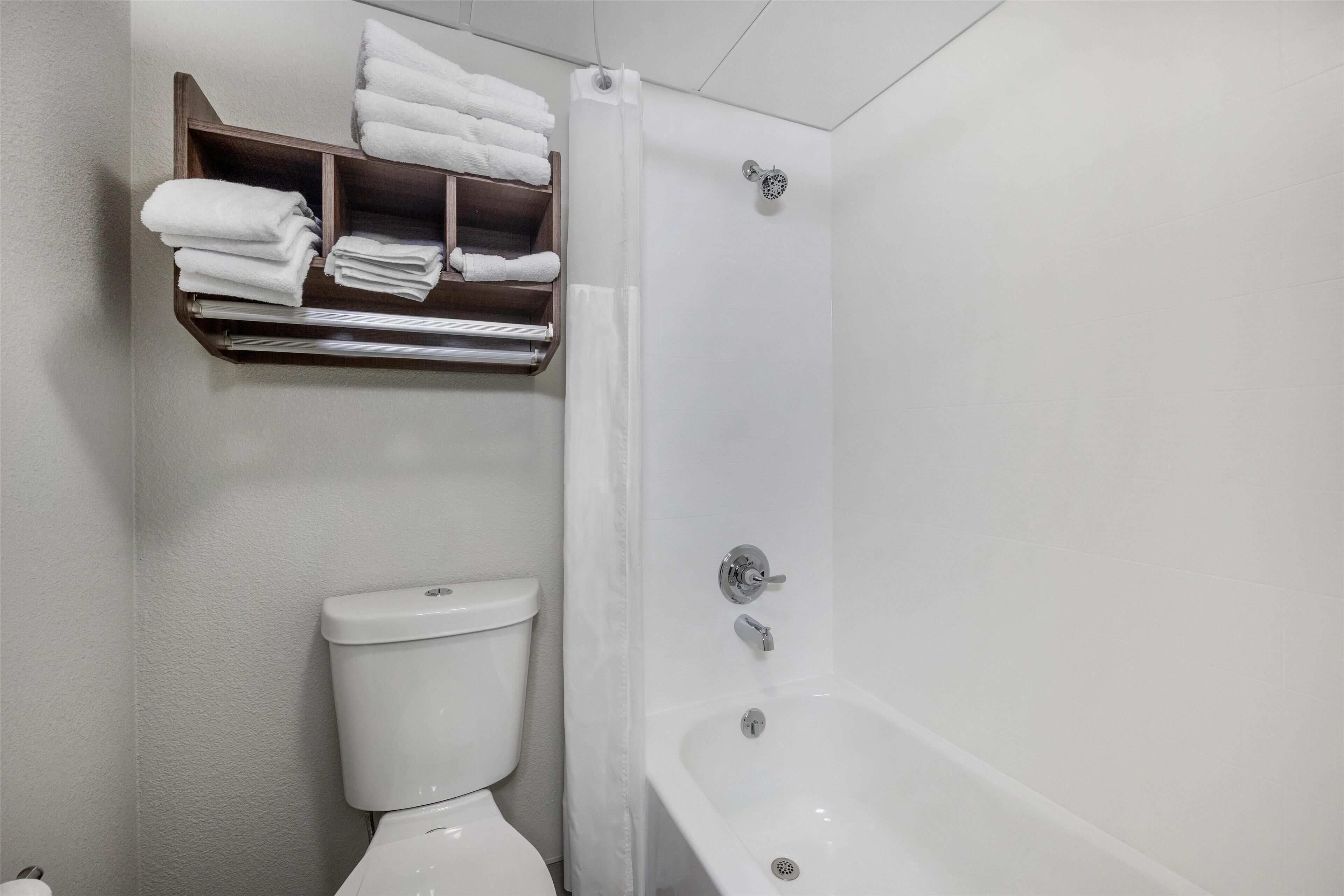 A bathroom with a toilet, a bathtub, and a shelf with folded towels.