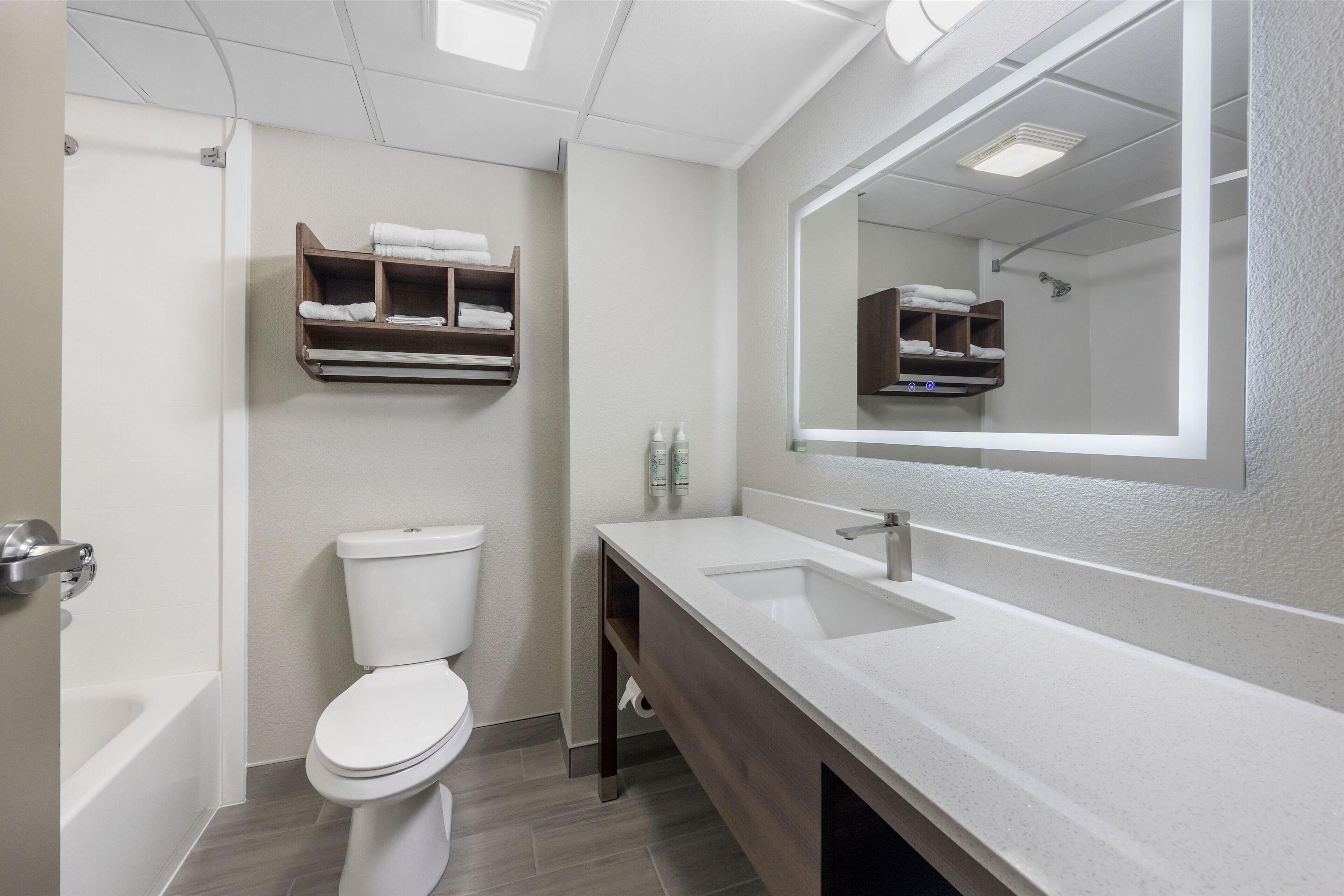 A modern bathroom with a toilet, a sink, a mirror, and a shelf with towels.