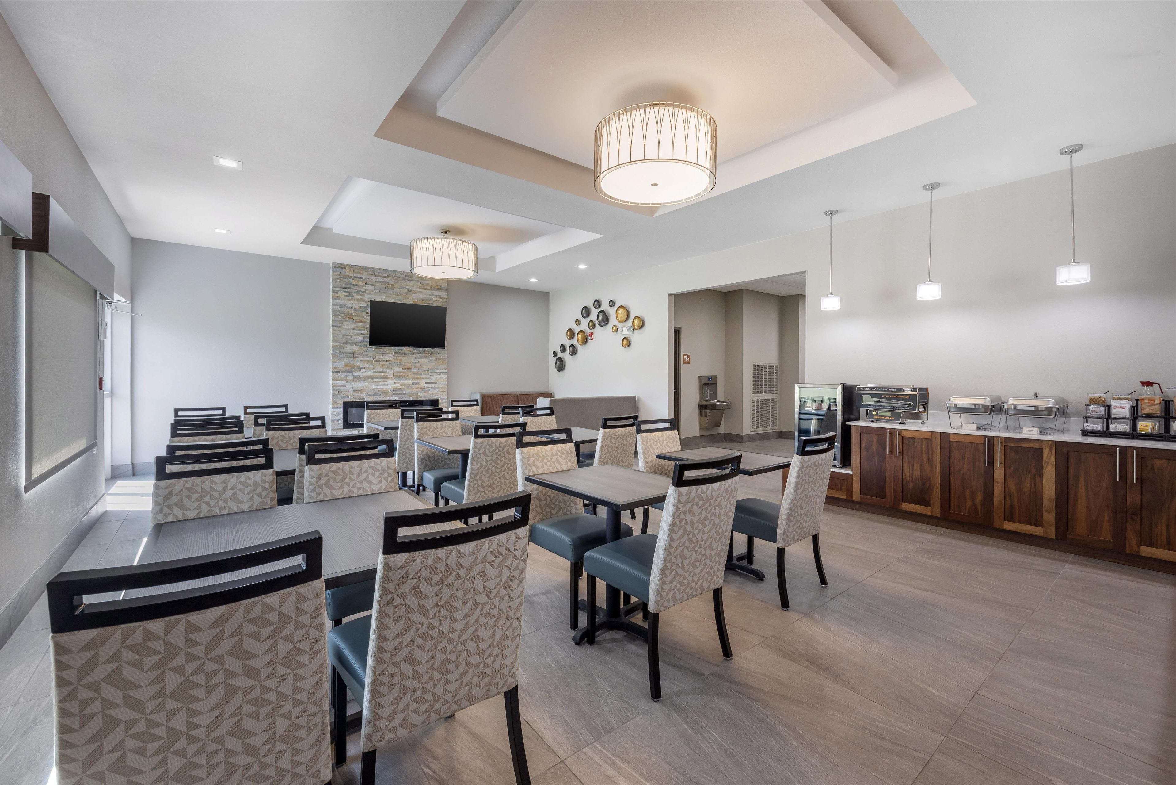 A modern dining area with multiple tables and chairs, a stone accent wall, and a buffet counter.