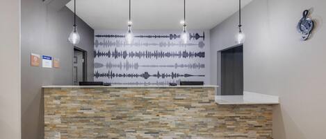 Uma área de recepção com balcão de textura de pedra, iluminação pendente e um mural com o tema de ondas sonoras na parede.