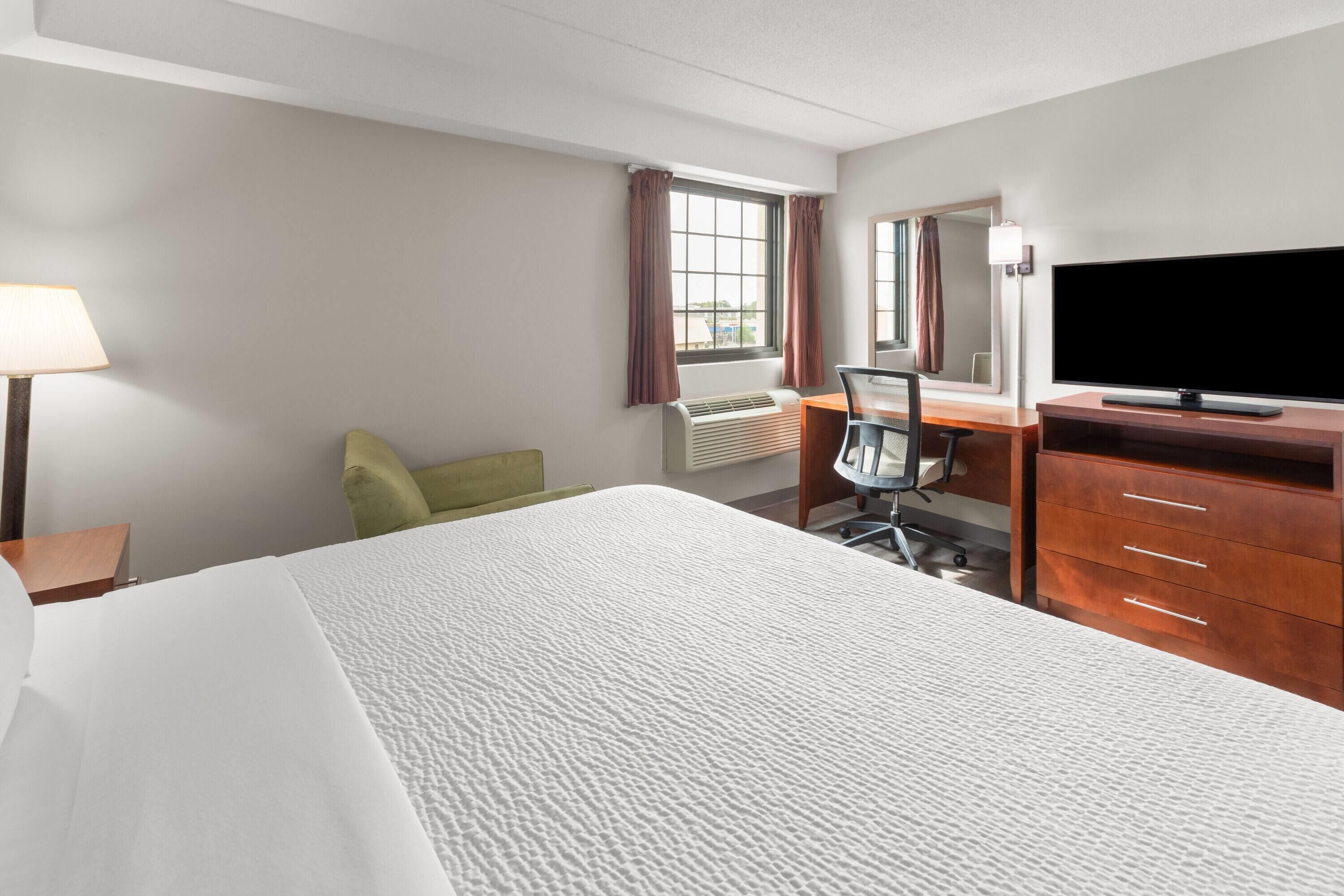 A hotel room with a bed, a desk, a chair, a television, a lamp, and a window with curtains.