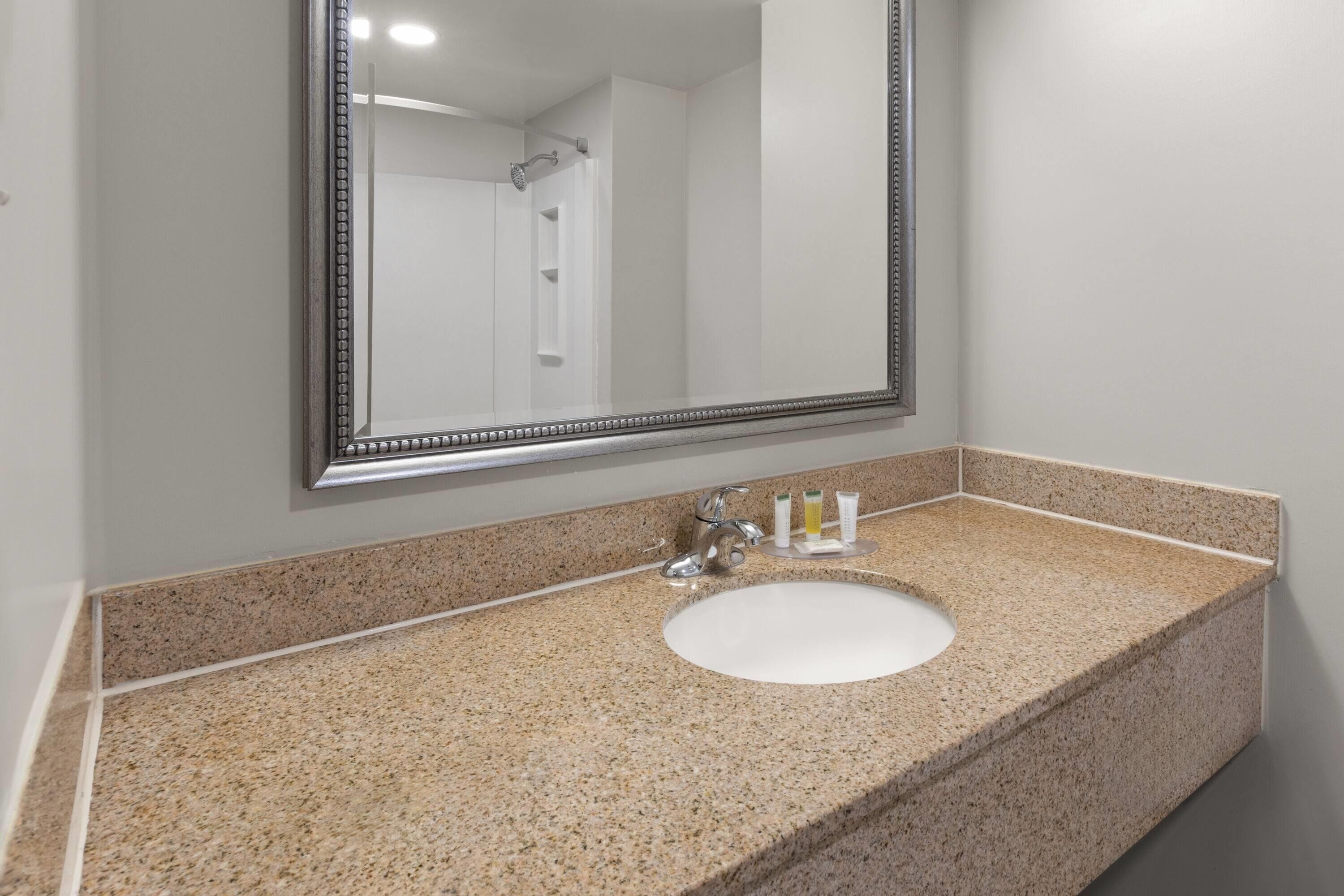 Un baño con encimera de granito, lavamanos blanco y un espejo grande.