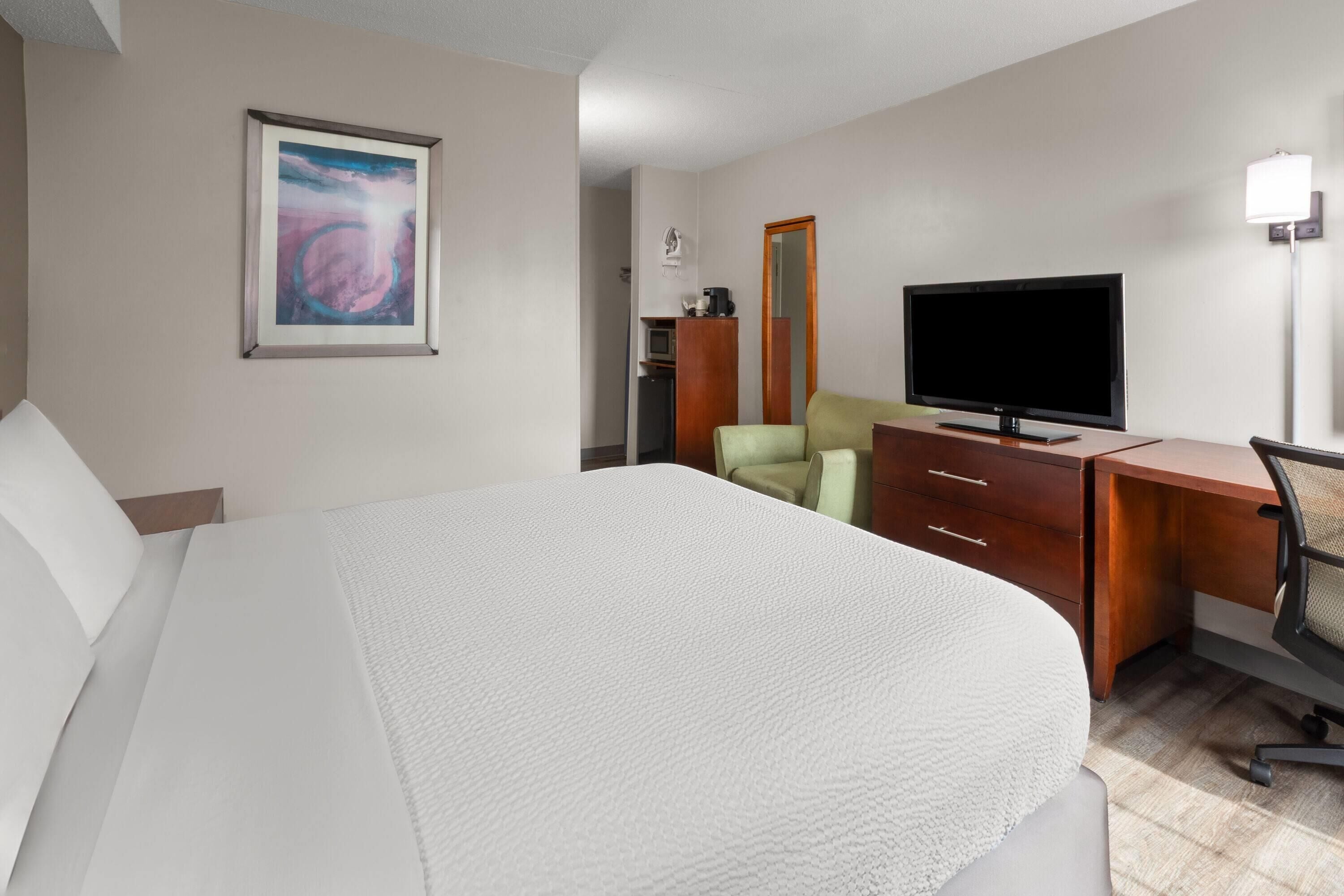 Habitación de hotel con una cama grande, un escritorio con televisor, una silla y un cuadro en la pared.
