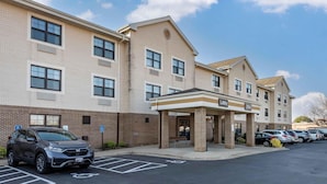 A multi-story hotel with a brick facade, a covered lobby entrance, and a parking lot with several cars.