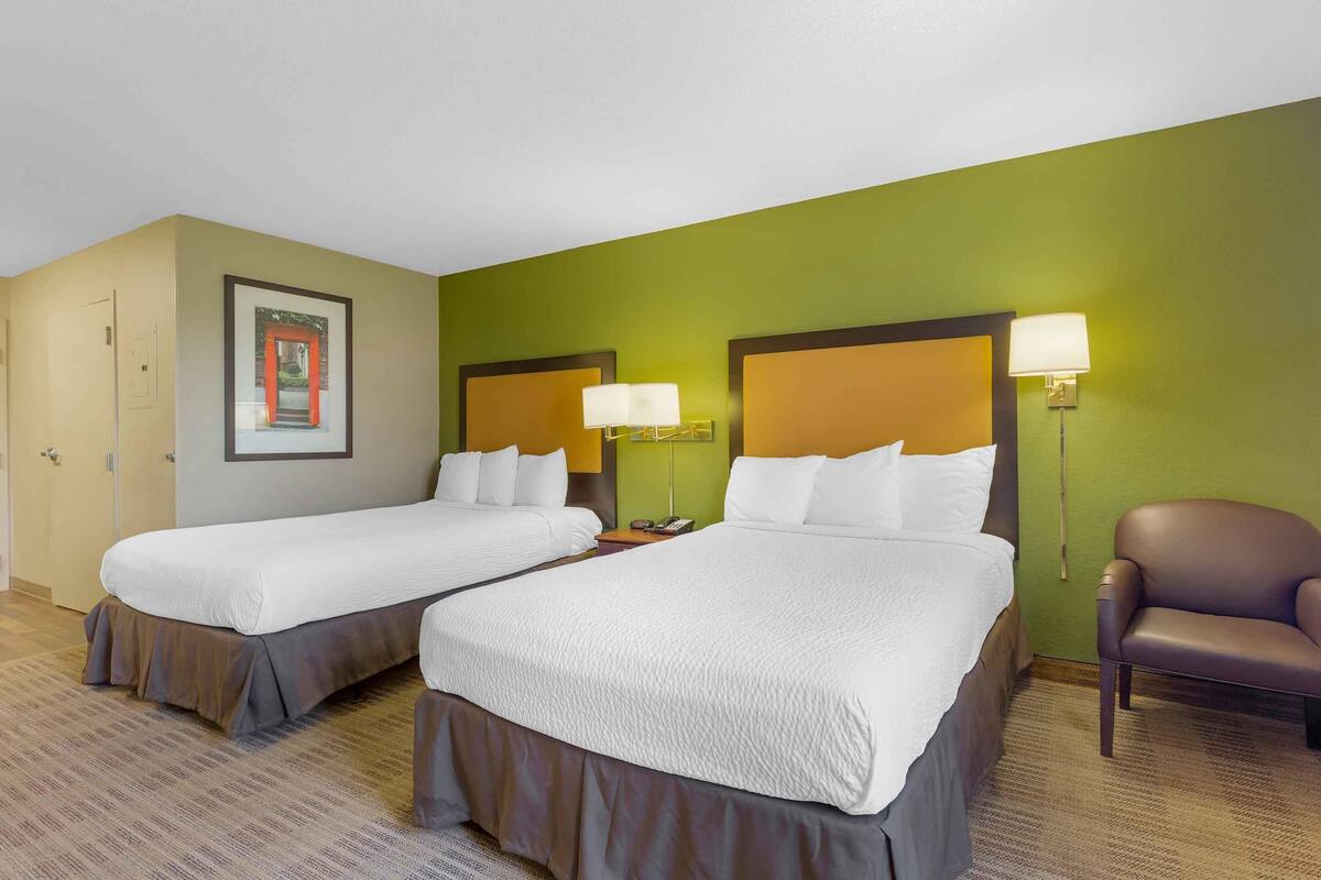 A hotel room with two beds, a chair, and a framed picture on the wall.