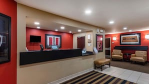 A hotel reception area with a black reception desk, a 'WELCOME' sign, a bench, and two armchairs.