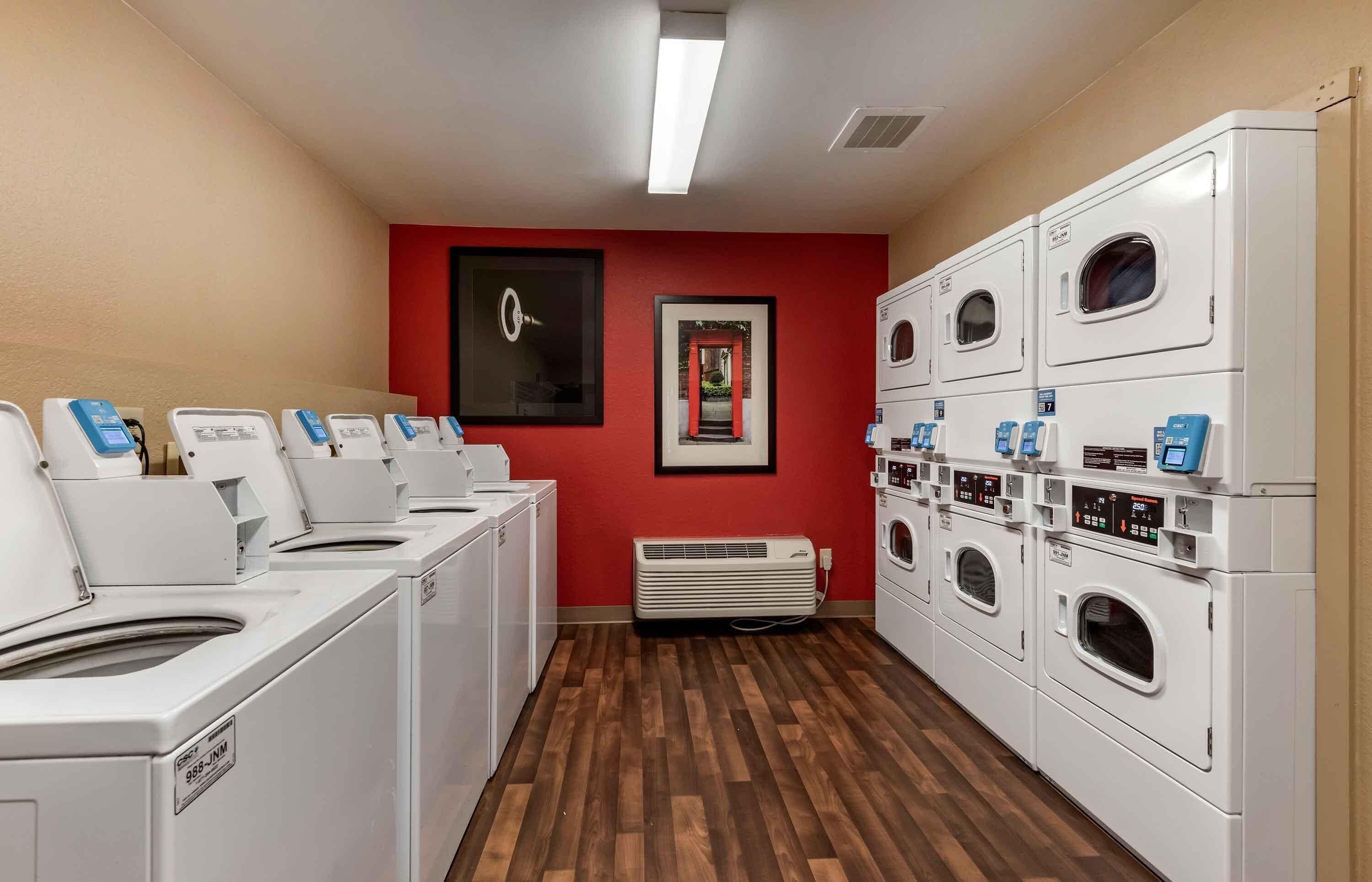 A laundry room with multiple washing machines and dryers, a red wall, and a framed picture.