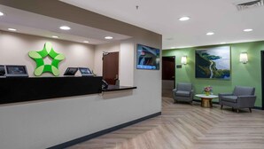 A reception area with a modern desk, two armchairs, a wall-mounted TV, and a painting. - Extended Stay America Suites Red Bank Middletown (Red Bank)