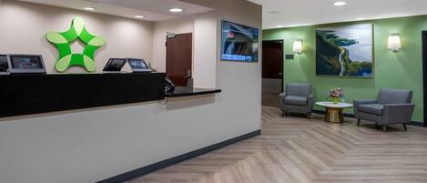 A reception area with a modern desk, two armchairs, a wall-mounted TV, and a painting.
