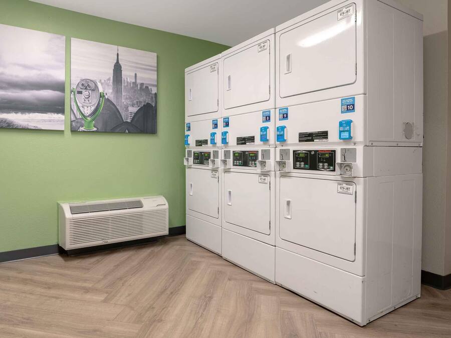 A laundry facility with multiple dryers, a wall-mounted air conditioner, and artwork depicting a lighthouse and a cityscape.