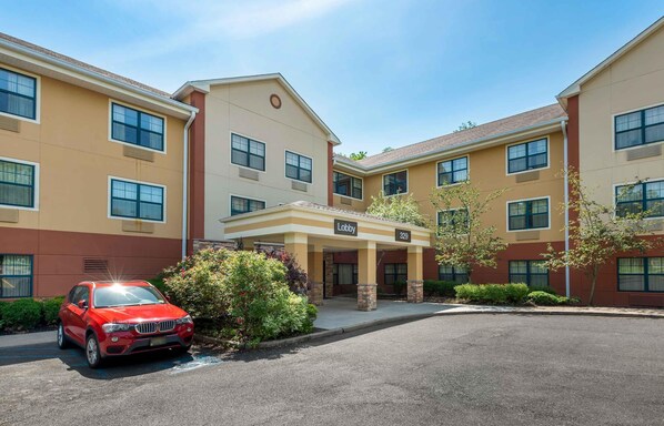 A multi-story hotel with a lobby entrance, numbered 329, and a red car parked in front.