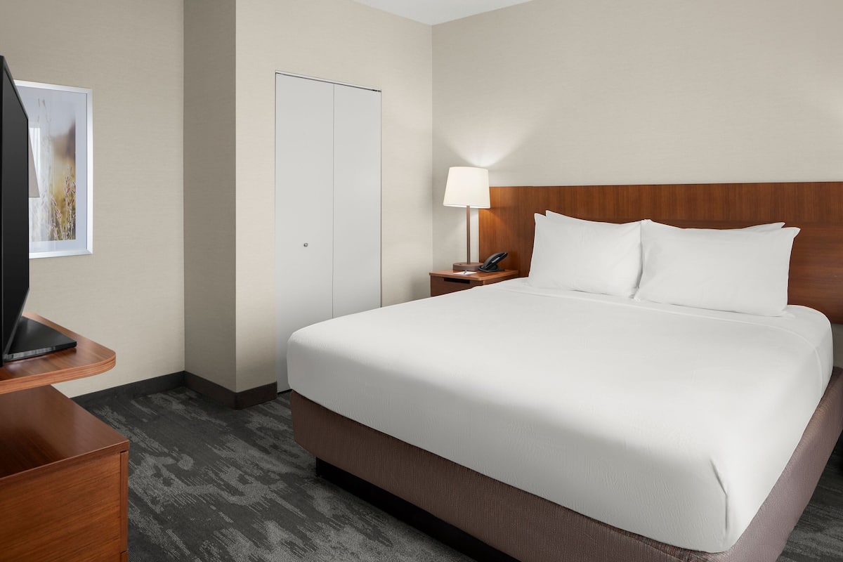 A hotel room with a large bed, a bedside table with a lamp, a telephone, and a TV on a stand.