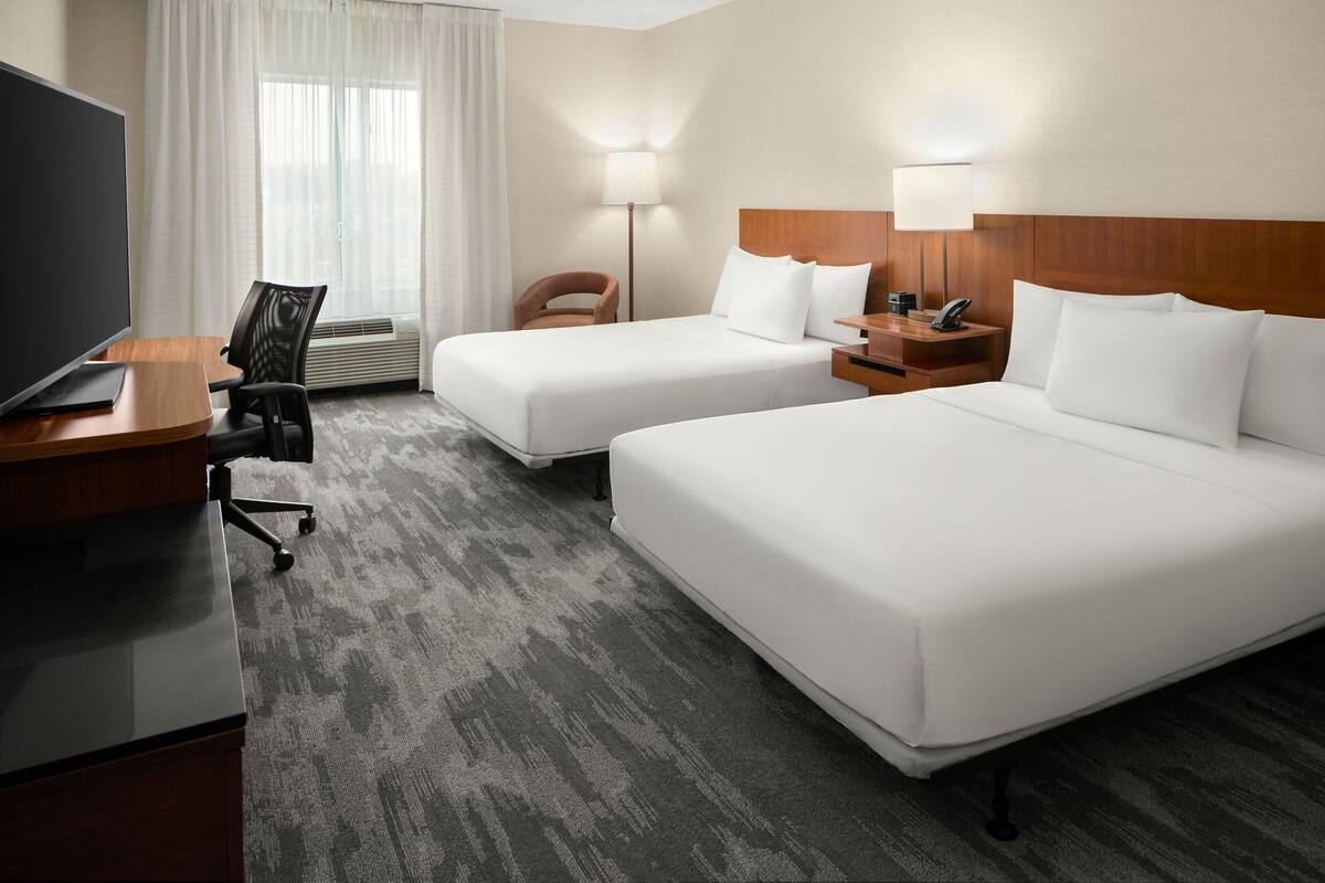 A hotel room with two beds, a desk with a TV, a chair, a lamp, and a bedside table with a phone.