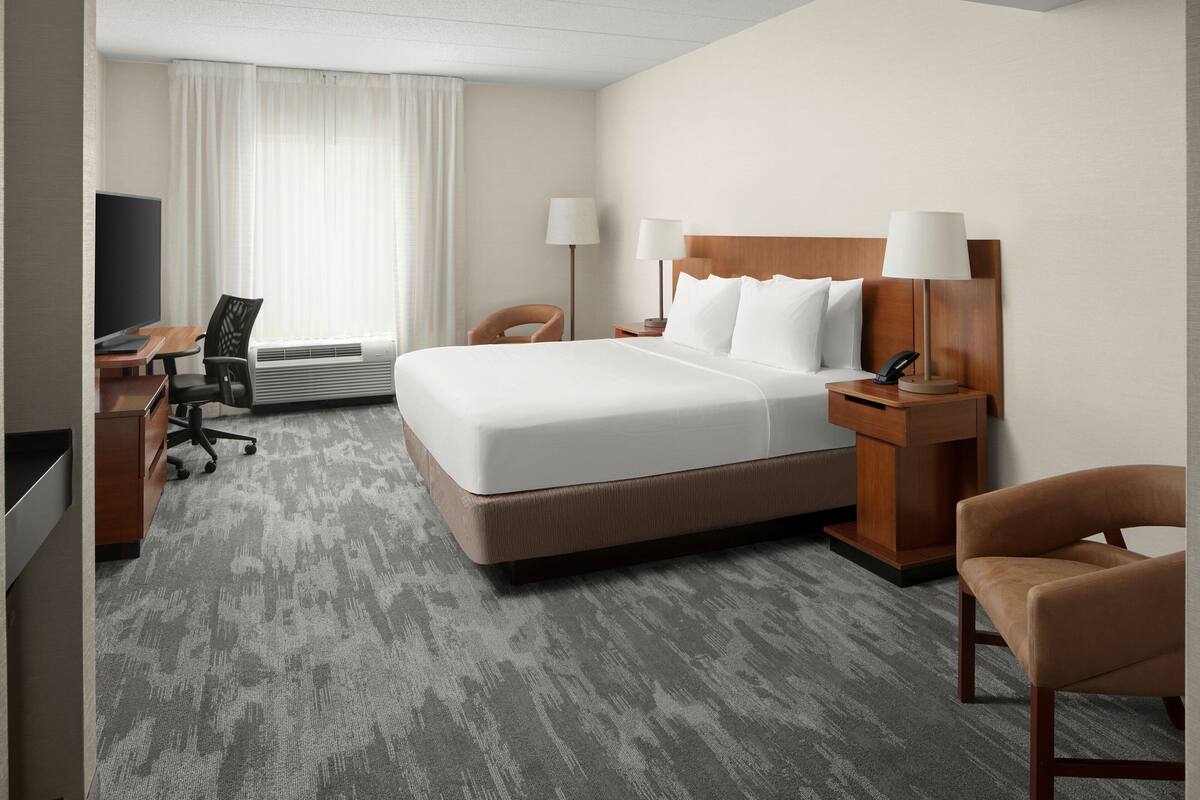 A hotel room with a large bed, a desk with a computer, a chair, and a TV.