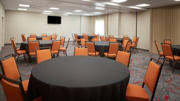 A conference room with multiple tables and chairs, a flat-screen TV on the wall, and a large window with curtains.