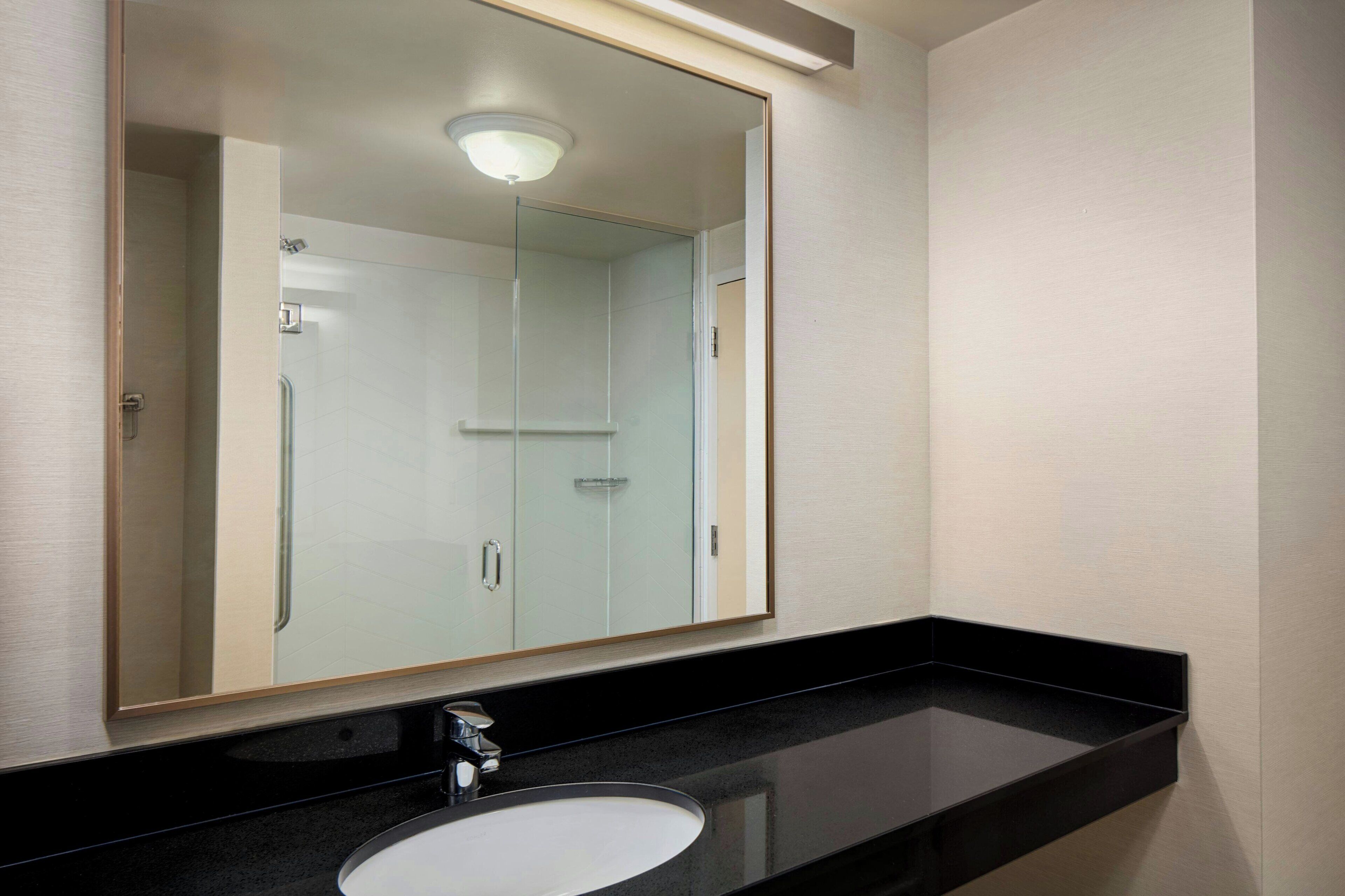 Un baño con un espejo grande, encimera negra y lavamanos blanco.