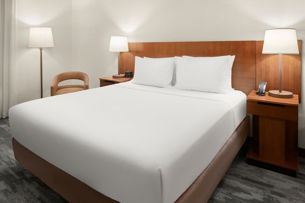 A hotel room with a large bed, two bedside tables with lamps, a chair, and a carpeted floor.