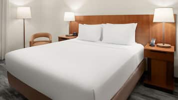 Ein Hotelzimmer mit einem großen Bett, zwei Nachttischen mit Lampen, einem Sessel und Teppichboden.
