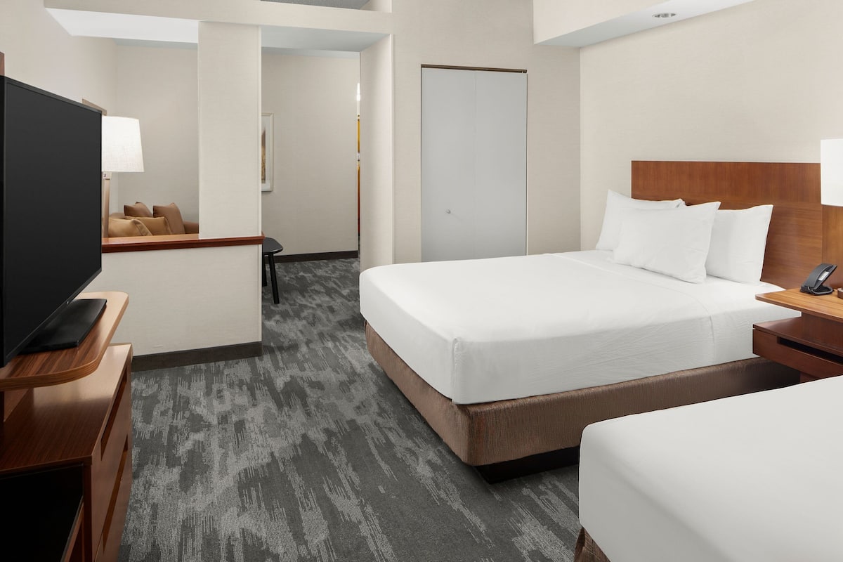 A hotel room with a large bed, a TV on a wooden stand, a desk with a lamp, and a door leading to another room.
