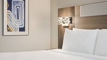 Una habitación de hotel con una cama bien hecha, una obra de arte moderna en la pared y una lámpara fijada a la pared.