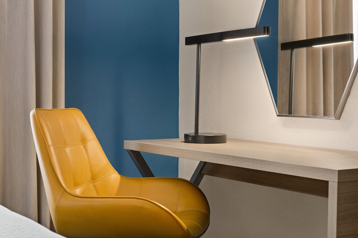 Una habitación moderna con un sillón de cuero amarillo, un escritorio de madera y una lámpara de escritorio negra.