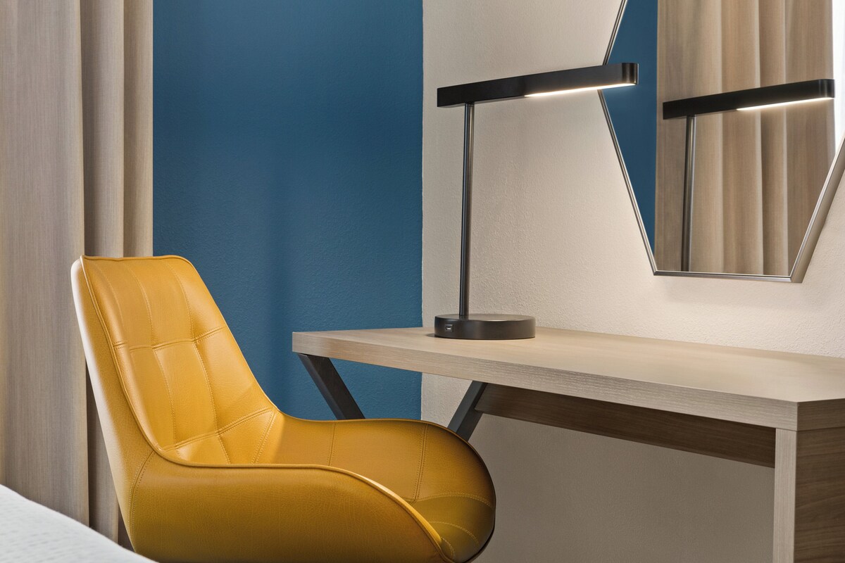 Una habitación moderna con un sillón de cuero amarillo, un escritorio de madera y una lámpara de escritorio negra.