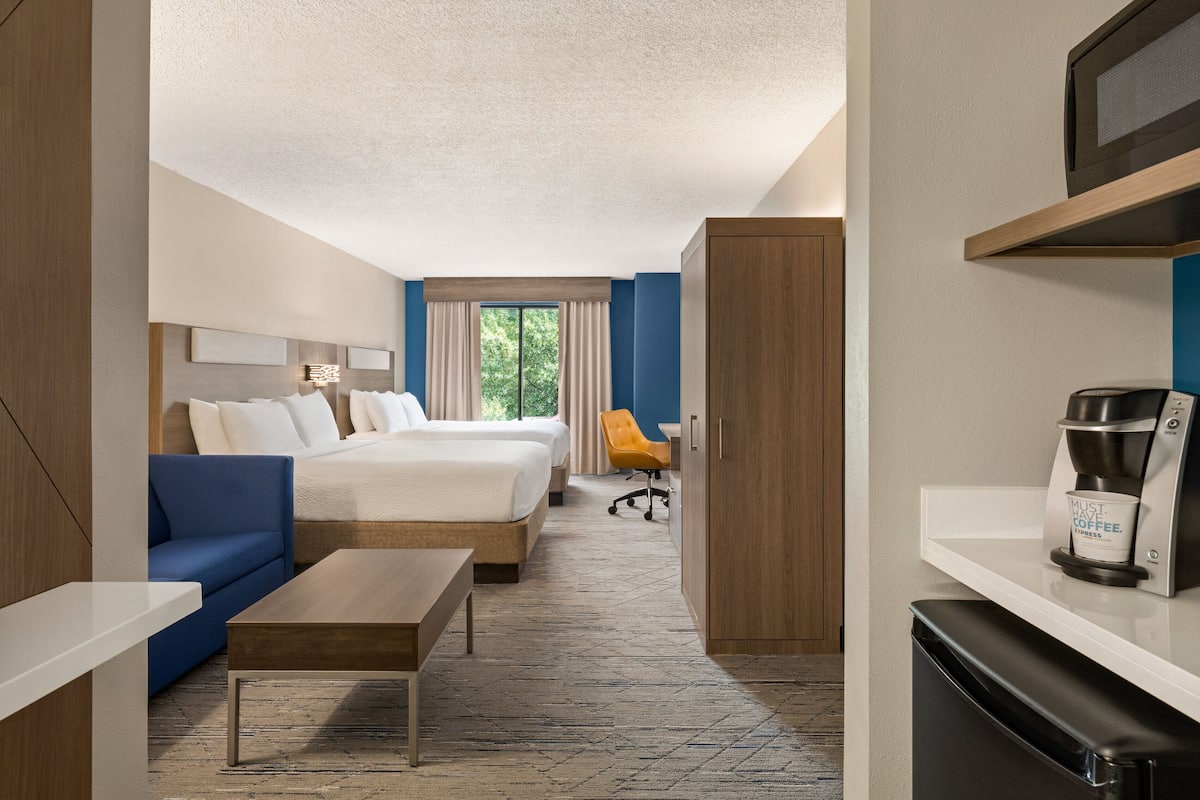 Habitación de hotel con cama, sofá, escritorio, cafetera y vistas a zonas verdes.