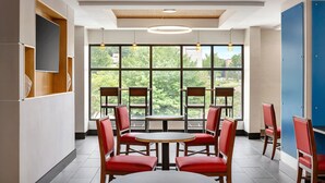 A modern interior with a round table and red chairs, large windows with a view of greenery, and a blue door. - Holiday Inn Express & Suites Greenville - Downtown by IHG (Greenville)