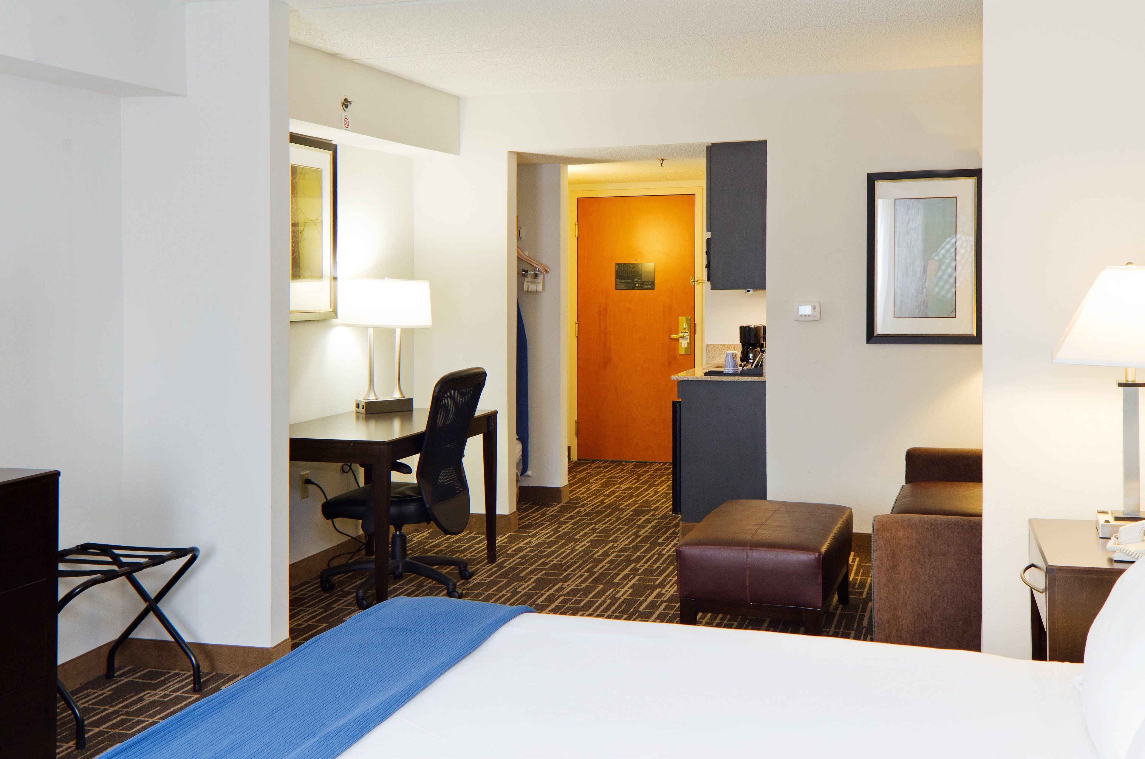 Een hotelkamer met een bed, bureau, stoel en een kleine kitchenette.