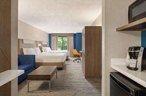 Une chambre d’hôtel équipée d’un lit, d’un canapé, d’un bureau, d’une machine à café et offrant une vue sur la verdure environnante.