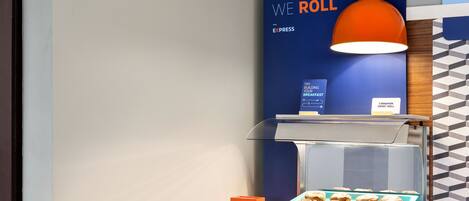 A breakfast station with a sign reading "THIS IS HOW WE ROLL" and a display case with pastries.