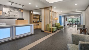 A hotel lobby with a reception desk, seating area, and a view of the outdoors. - Holiday Inn Express & Suites Greenville - Downtown by IHG (Greenville)