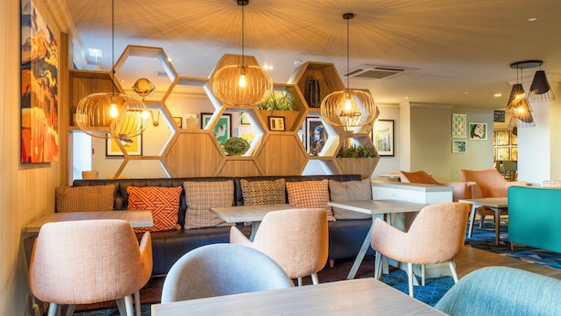 A modern hotel lobby with hexagonal wooden partitions, comfortable seating areas, and contemporary lighting fixtures.