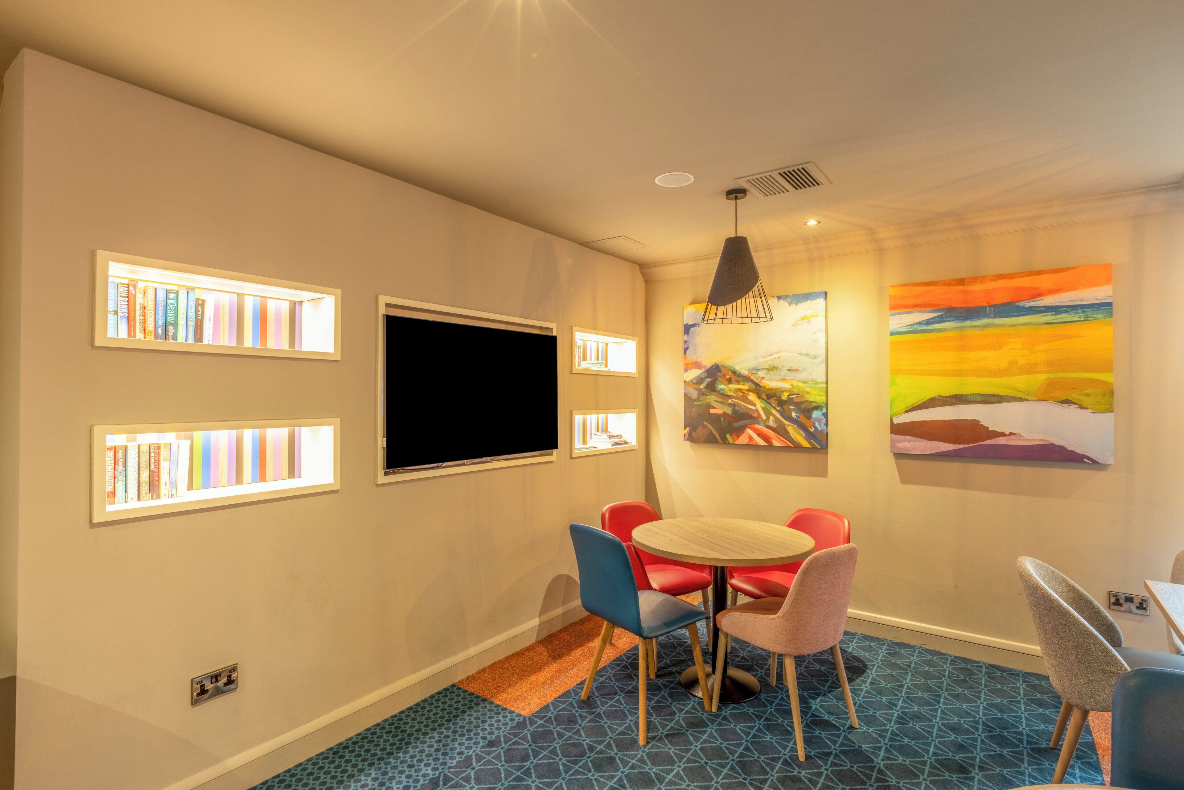 A room with a round table, chairs, bookshelves, a flat-screen TV, and artwork on the walls.