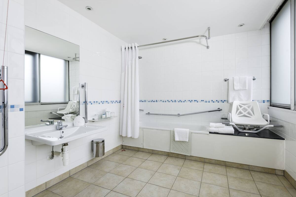 Une salle de bain moderne équipée d’un lavabo, d’un miroir, d’une douche et d’un banc accessible aux personnes en fauteuil roulant.
