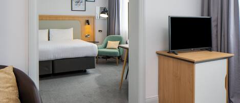 Habitación de hotel con una cama, un escritorio con televisor, una silla y un sofá.