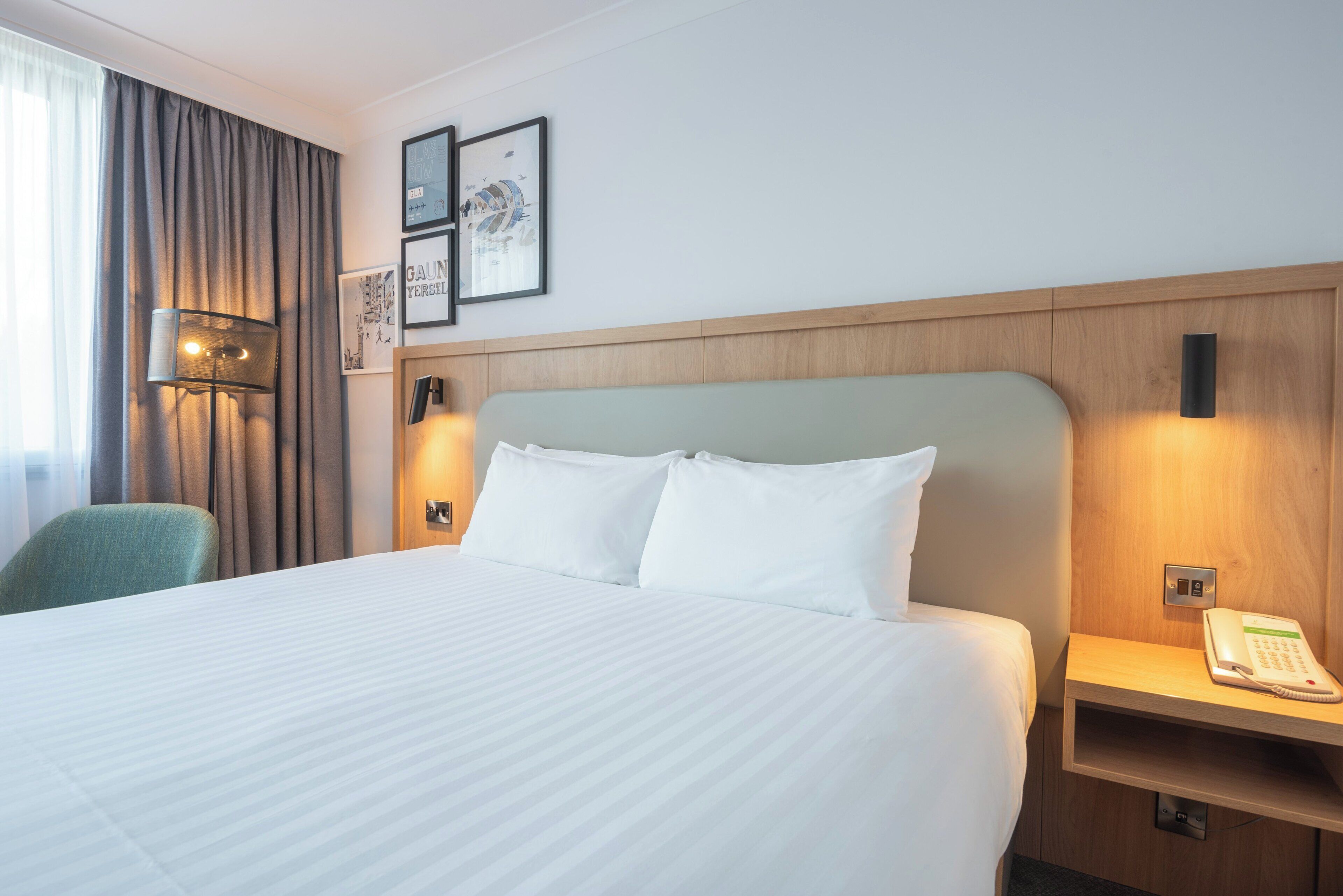 A hotel room with a large bed, a desk with a telephone, a chair, and a wall-mounted lamp.
