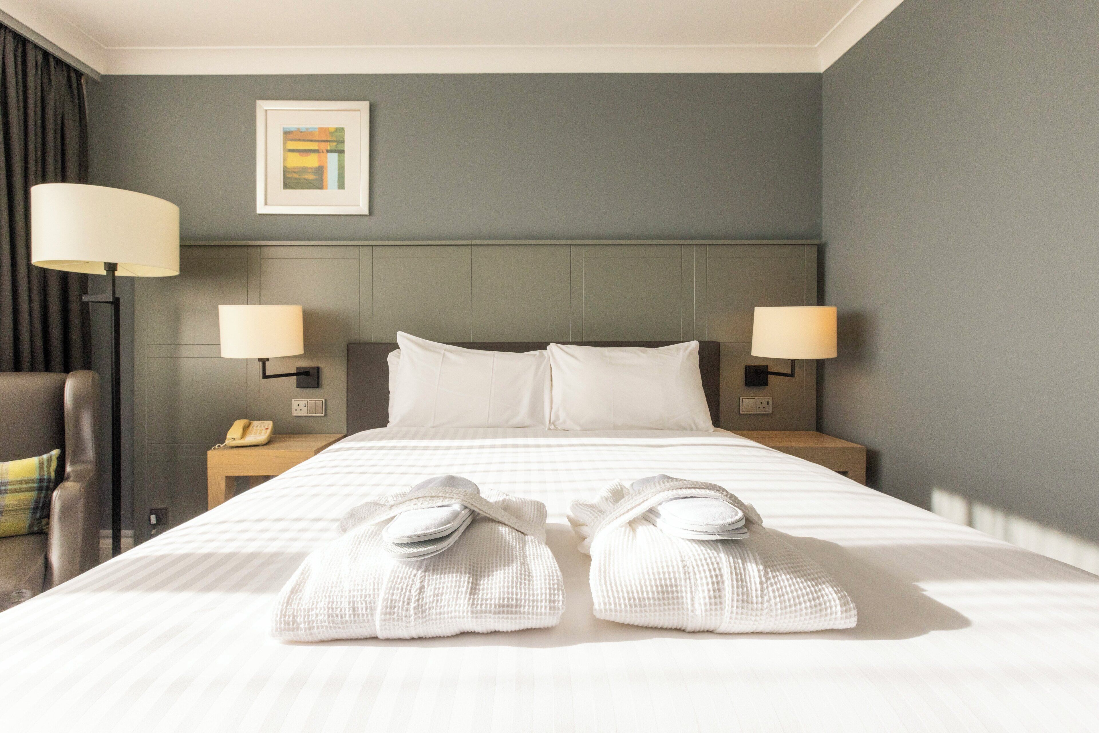 Habitación de hotel con una cama grande, dos lámparas de noche, un teléfono y un cuadro en la pared.