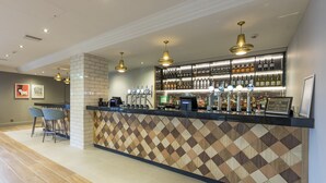 A modern bar area with a patterned wall, multiple beer taps, and a seating area with chairs.