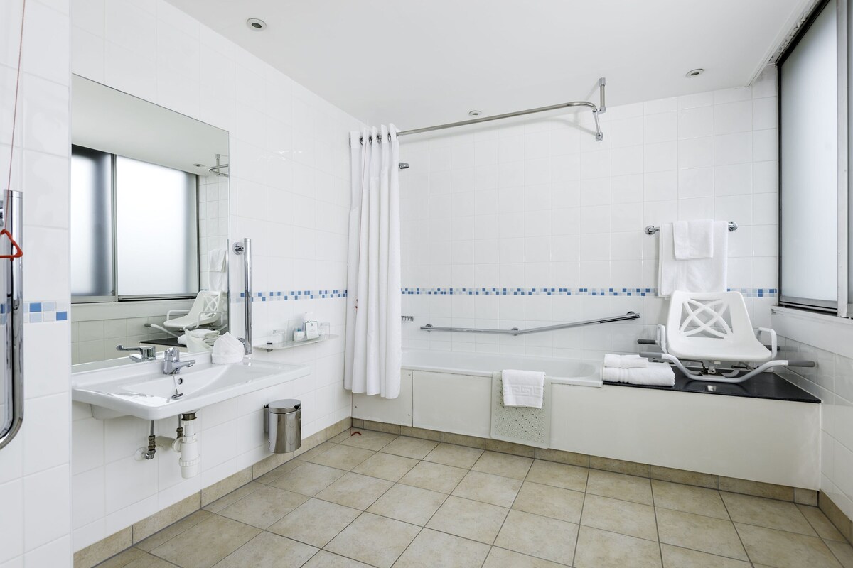 Un baño moderno con lavamanos, espejo, ducha y un banco accesible para sillas de ruedas.